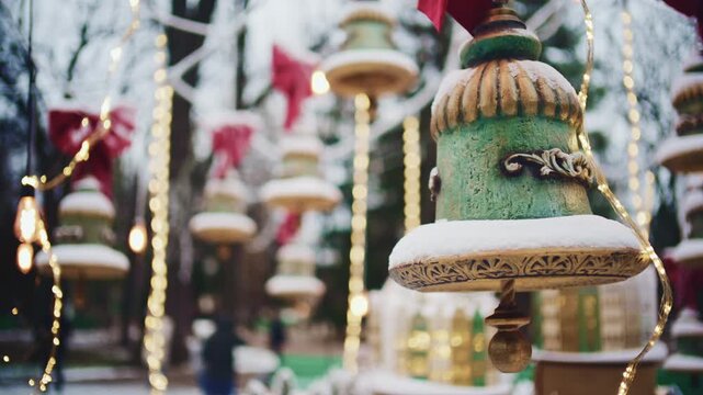 Close up of decorative hanging ornaments covered with snow and surrounded by warm string lights in an outdoor winter setting
