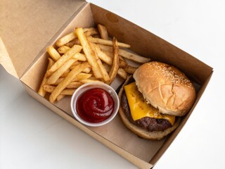 Cheeseburger and french fries packed neatly in a brown kraft paper box with ketchup dip on the side topdown view for gourmet food presentation