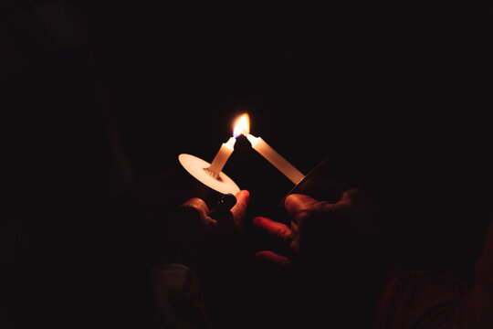 Hands lighting white candle from another flame in total darkness