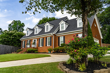 Two story red brick house with dormer windows and green lawn