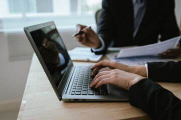Fototapeta premium Two business people are discussing and analyzing financial charts and reports at their desks in an office, with laptops nearby. The atmosphere is serious and professional.