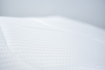 Detailed view of a pristine white quilted mattress protector or topper. The surface shows a subtle pattern of small, raised dots in rows, highlighting its soft texture