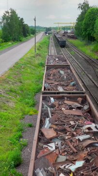 Vertical. Long line of scrap wagons stretches along rails beside country road