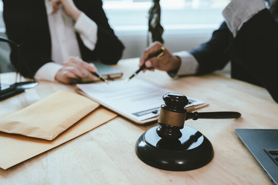Two lawyers discuss legal documents at a desk, with a scale of justice and gavel symbolizing law, authority, and professional legal consultation in a modern office.