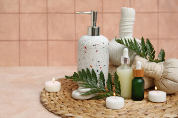 Set of spa supplies with bottles of cosmetic oil, herbal bags, fern branches and burning candles on beige table