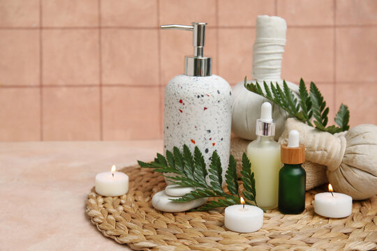Set of spa supplies with bottles of cosmetic oil, herbal bags, fern branches and burning candles on beige table