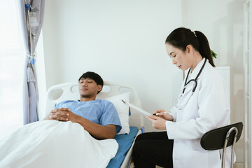 Obraz premium Female doctor reviewing medical records on a clipboard while a male patient rests in a hospital bed during inpatient care.