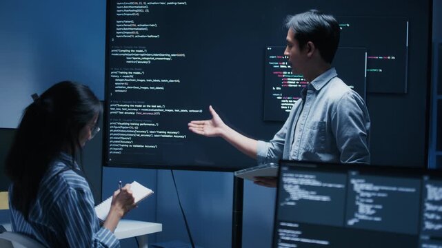 Male software engineer presenting a Coding Task, AI chatbot workflow with code on multiple monitors in a modern office. coding collaboration and agile projects Concept.