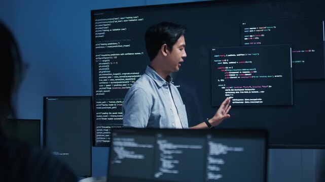 Asian Male software engineer pointing at source code on a large screen during a tech team meeting, explaining Code on the Screen, Discussing on coding task, New software development project in office.