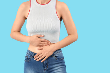 Young beautiful woman suffering from abdominal pain on blue background, closeup