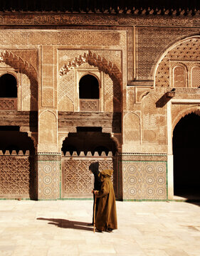 Men walking past a traditional wooden lattice screen in the courtyard of the Medersa Bou Inania in Fez, Morocco
