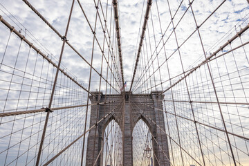 Fototapeta premium Brooklyn Bridge pedestrian walkway perspective with suspension cables and stone towers against cloudy sky in New York City USA