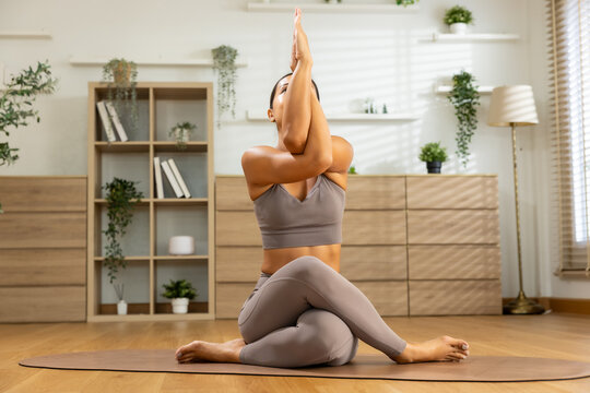 Calm woman performing eagle pose during yoga workout session on floor mat in bright living room practicing mindfulness wellness flexibility