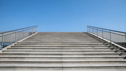 Fototapeta premium Long staircase with metal handrails leading up to clear blue sky on sunny day