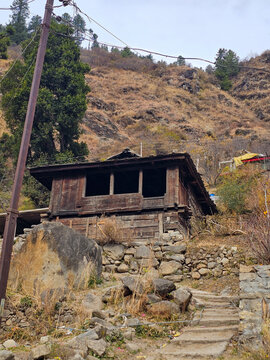 Vertical View of Traditional Old Wooden House Built on Steep Rocky Slope with Stone Foundation and Utility Pole in Himalayas Himachal Pradesh India.