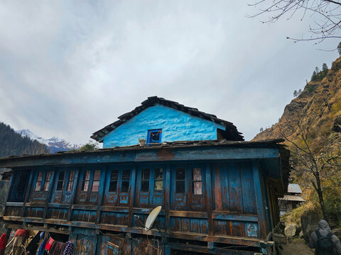 Horizontal Landscape View of Traditional Two-Story Himalayan Wooden House with Vibrant Blue Painted Upper Floor and Slate Roof in Himachal Pradesh India.
