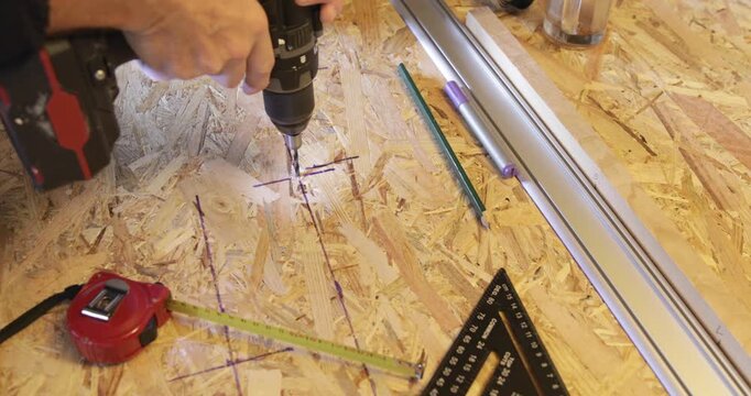 Carpenter drilling hole at OSB panel using cordless electric drill 
