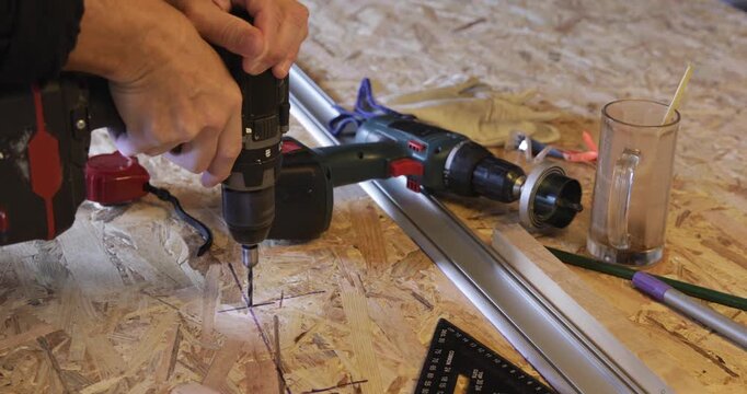 Carpenter drilling hole at OSB panel using cordless electric drill 