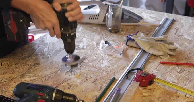 Carpenter - woodworker cuts hole through OSB plate using cordless drill and circular hole saw attachment and dusting sawdust using vacuum cleaner