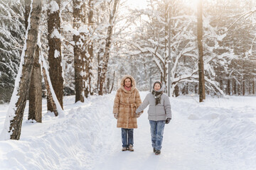 Fototapeta premium Walking mother with teen son on snowy forest road, tall trees, calm winter landscape, family time, bonding, childhood memory, outdoor activity, healthy lifestyle, weekend leisure, holiday mood.