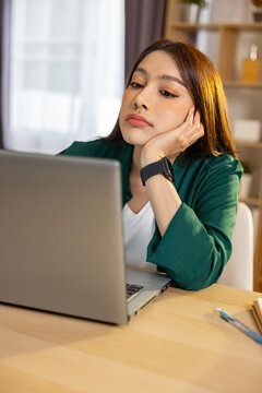 Portrait of bored asian woman feeling tired and unmotivated while working on laptop computer at home office desk looking away with unhappy and exhausted expression Vertical