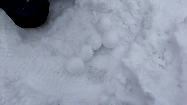 A child makes snowballs with a red plastic snowball maker. A boy prepares many snowballs for a snowball fight