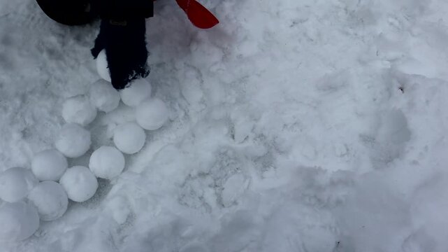 A child makes snowballs with a red plastic snowball maker