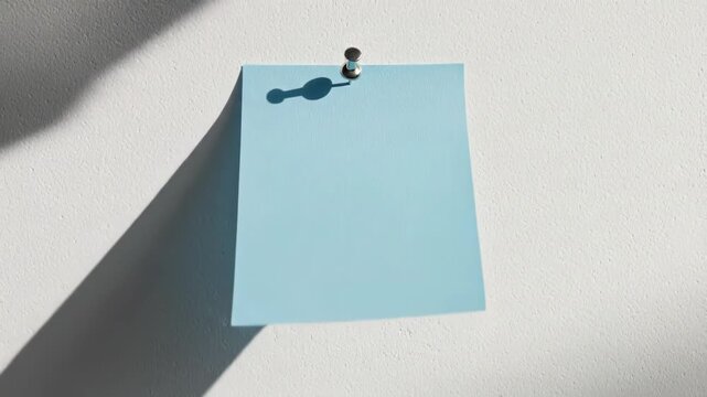 Blank blue sticky note pinned to a white textured wall with a metal push pin.