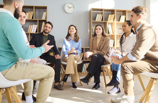 People group of adults in circle discussion. Supportive team listens during coaching in a bright library with chairs, building support and communication. Unity and teamwork theme now.
