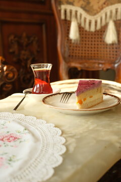 A slice of delicious fruit and berry mousse cake served with traditional Turkish black tea on an ornate vintage marble table under warm sunlight.