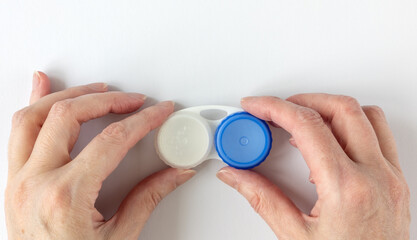 Fototapeta premium Woman's hands holding a contact lens case. Empty white plastic lens case with compartments for storing contact lenses