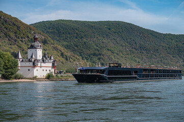 River cruise ship sailing along the Rhine River past the historic Pfalzgrafenstein Castle near Kaub with steep vineyard-covered hills of the Upper Middle Rhine Valley.