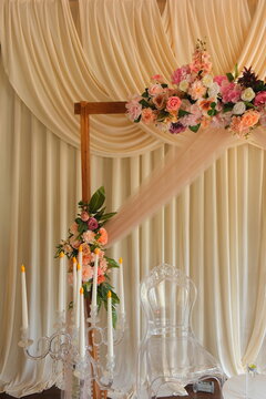  Elegant wedding photo zone decoration with pastel flowers, wooden arch, draped beige curtains, and crystal candelabra with artificial candles.