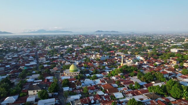 Beautiful aerial drone footage of the whole Mataram city valley, in Lombok island, Indonesia, at sunrise, with many big beautiful mosque, with many houses and trees