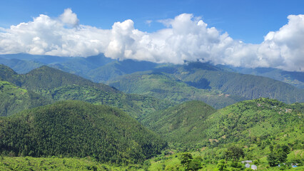 Obraz premium A magnificent panoramic view of verdant green mountains covered in dense forests under fluffy clouds.