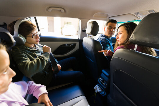 Parents arguing with their teenage son wearing headphones in the back seat during a family car trip