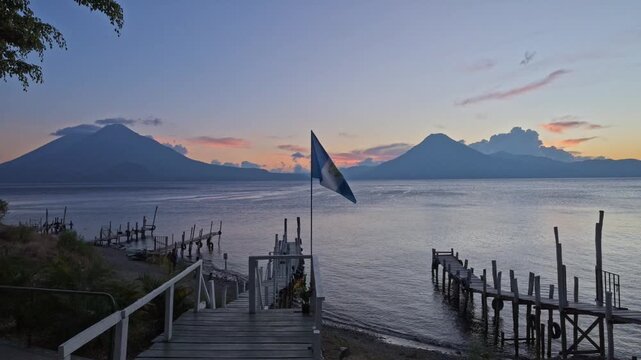 waving Guatemalan flag in front of volcanoes and sunset at Lake Atitlan and boat docks, Panajachel, Guatelmala, Central America