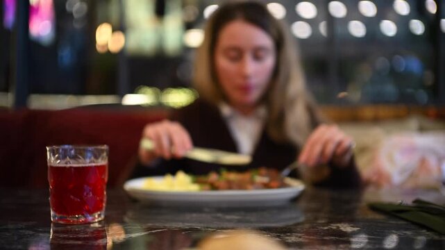 Woman eating mashed potatoes and meat at a restaurant table using fork and knife