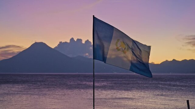 waving Guatemalan flag in front of volcanoes and sunset at Lake Atitlan, Panajachel, Guatelmala, Central America