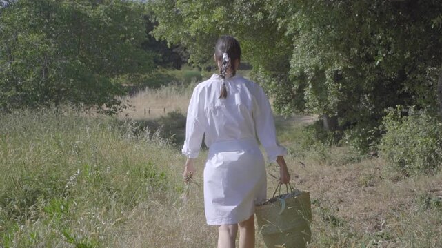 Young female in a white linen dress scouting the Mediterranean landscape with a straw basket for a sustainable and restorative travel concept