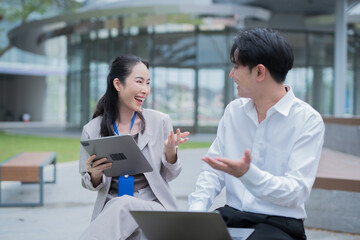 Obraz premium Two colleagues are smiling and working together on laptops at a modern desk.