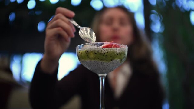 Woman eating a chia pudding dessert with fresh fruit toppings