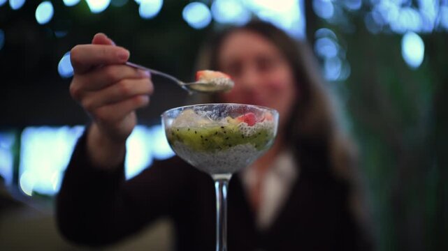 Woman eating a chia pudding dessert with fresh fruit toppings