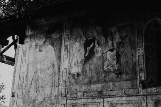Ancient religious frescoes on the exterior wall of St. Valentin church with wooden benches, South Tyrol, Italy