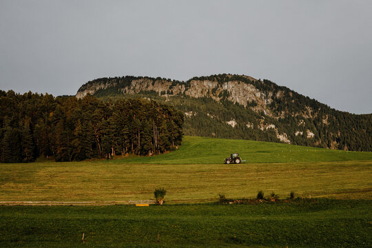 Black modern tractor transporting a wrapped silage hay bale on a green mountain meadow in South Tyrol