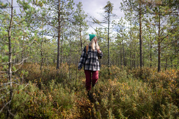 Obraz premium Middle aged woman explorer on weekend trip outdoors in wild autumn pine forest. Female hiker walking in fall marshy woodlands, enjoying sunlight and relaxing from daily life stress.