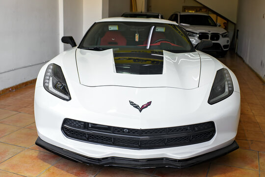 Msida, Malta - February 2, 2026: A close-up front view of a white Chevrolet Corvette C7 with a black hood stripe and the iconic crossed-flags logo inside a brightly lit showroom.