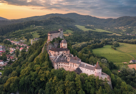 Orava Castle towering above a river valley under dramatic sunset sky highlighting medieval architecture and surrounding mountains.