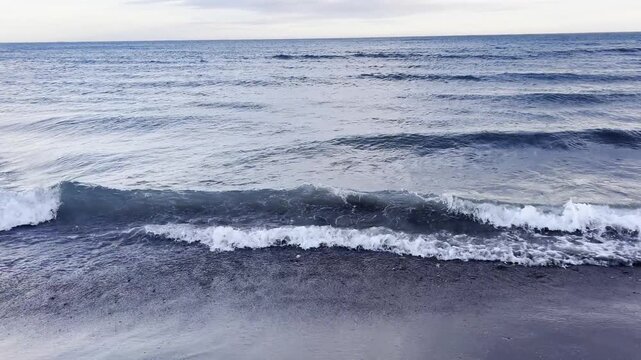 Ocean waves rolling onto dark sandy beach shore