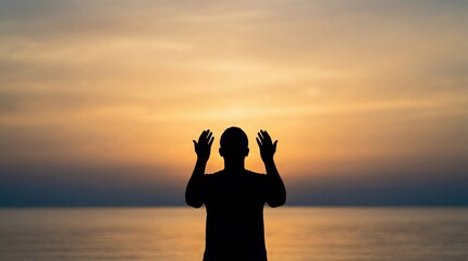 Fototapeta premium Silhouette of a man praying with hands raised towards the sunset over the ocean.